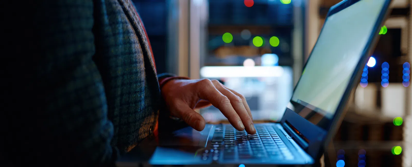 Person typing on a laptop in a dimly lit server room with glowing network equipment in the background
