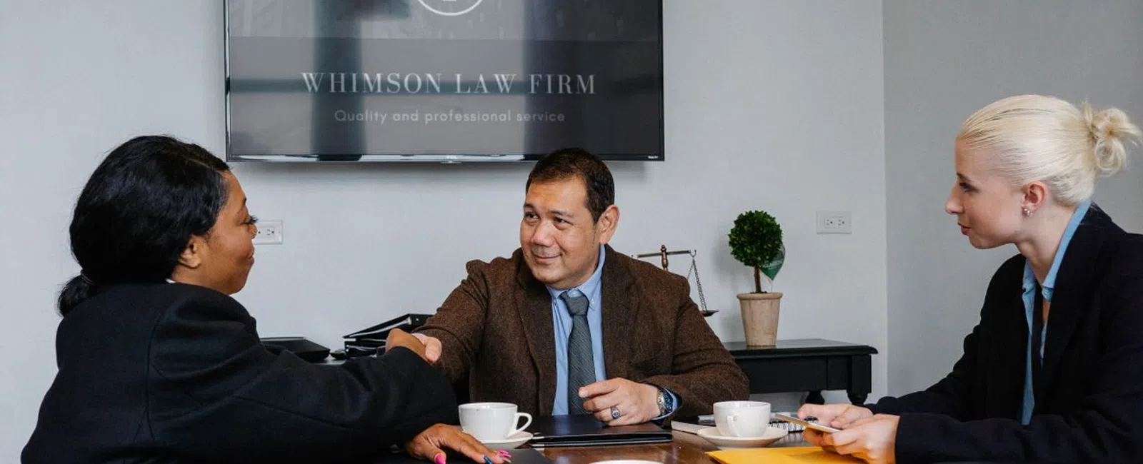 Lawyers shaking hands during a business meeting at Whimson Law Firm office with documents and coffee cups on the table