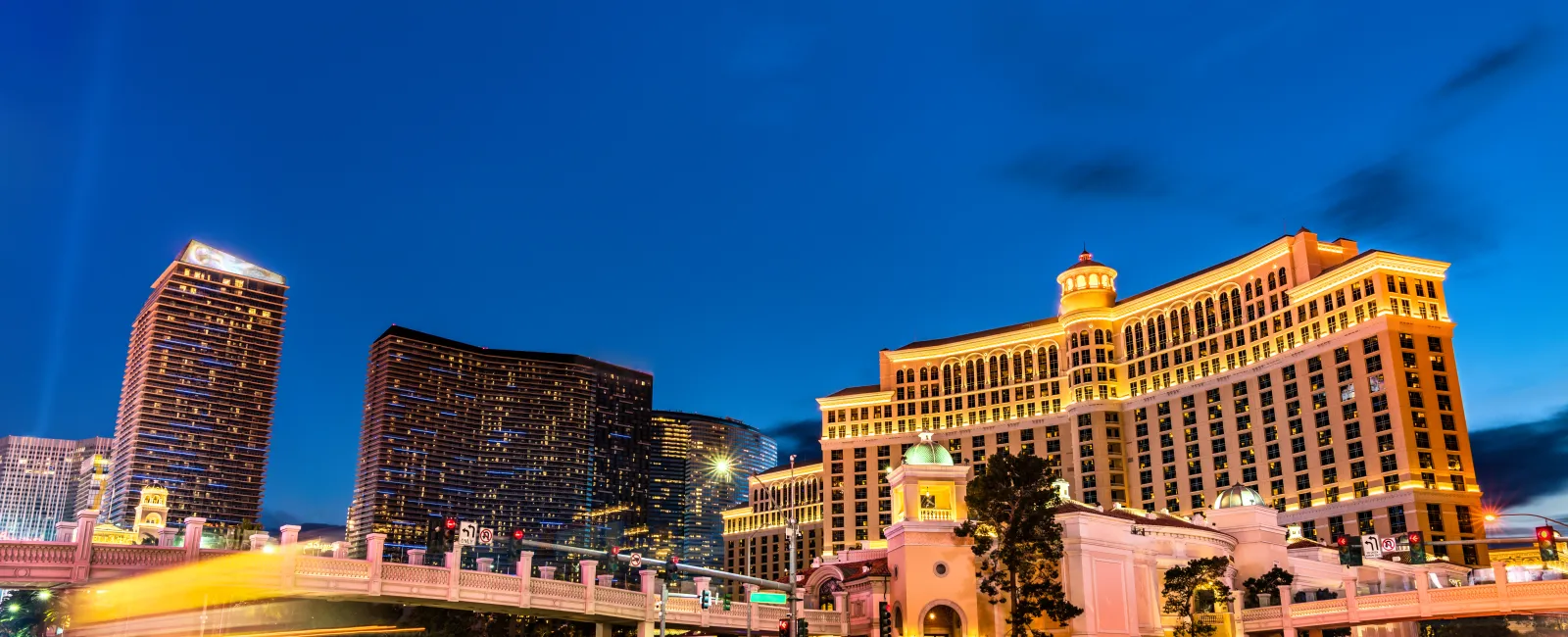 Night view of illuminated Bellagio Hotel and surrounding skyscrapers in Las Vegas with light trails on busy street.