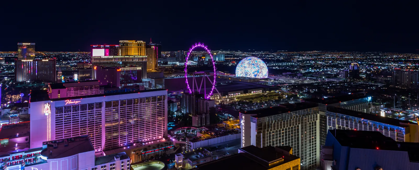 Las Vegas skyline at night with illuminated hotels, the High Roller Ferris wheel, and colorful city lights