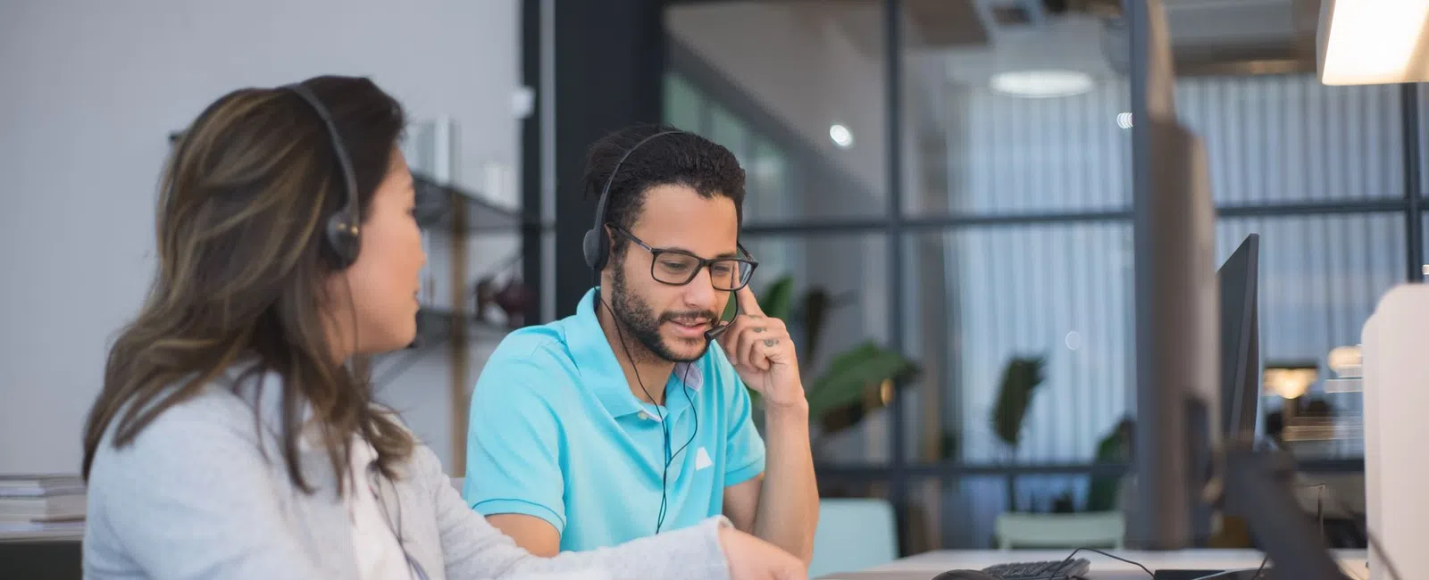 Two customer service agents wearing headsets working at computers in modern office setting