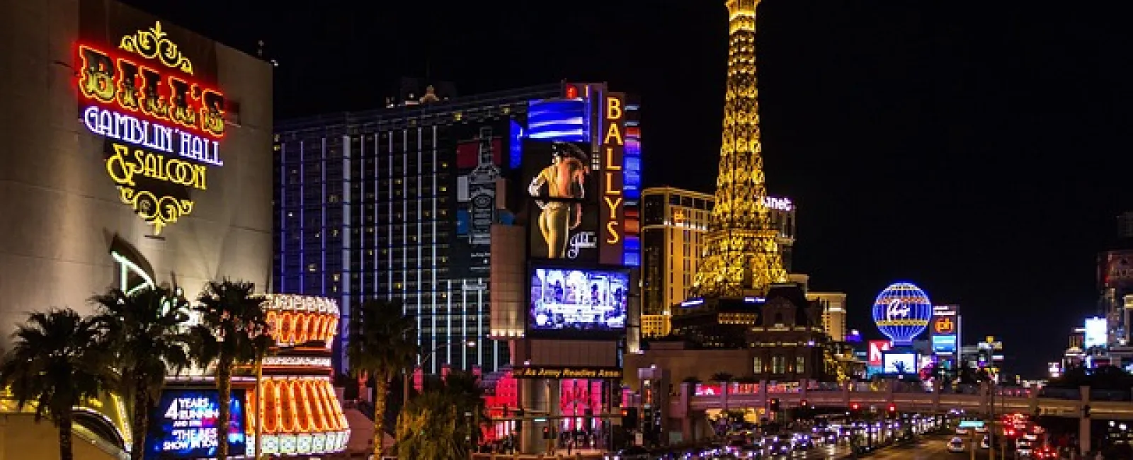 Nighttime view of vibrant Las Vegas Strip with illuminated signs, Eiffel Tower replica, and heavy traffic.