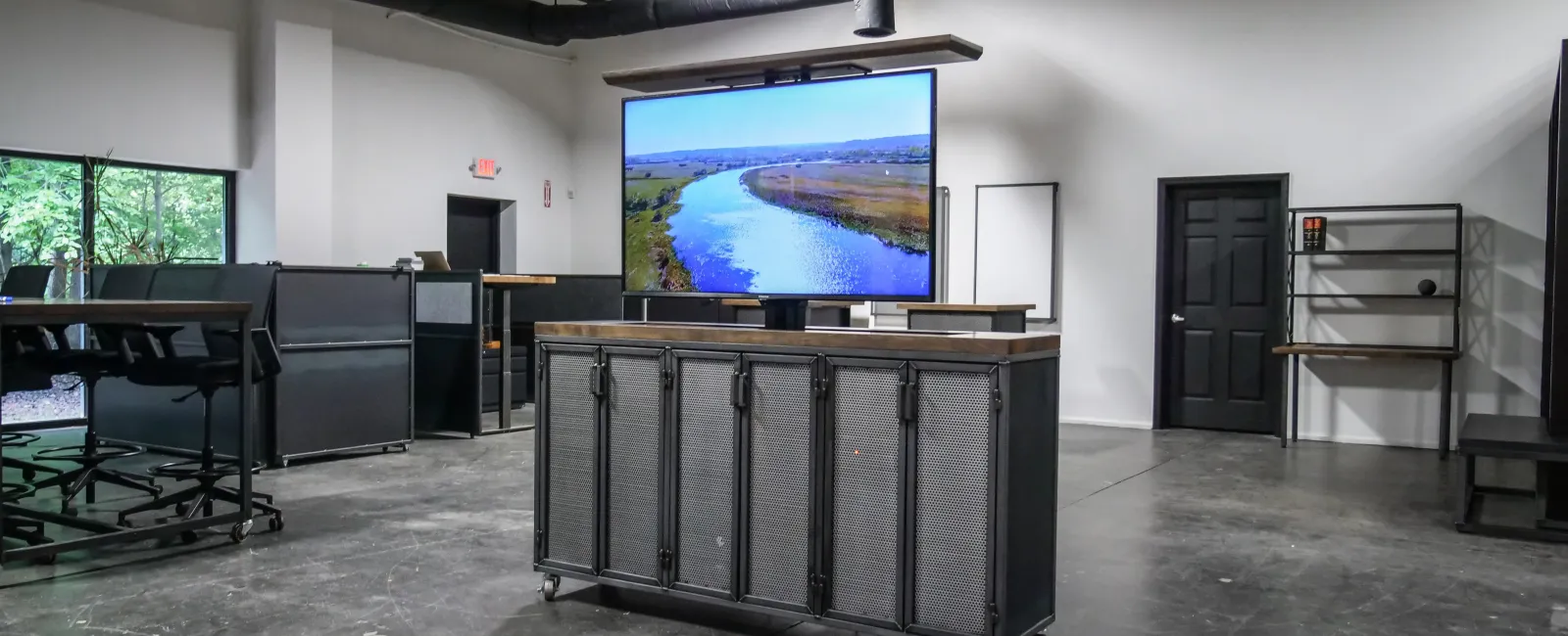Modern spacious office interior with black furniture, polished concrete floors, and a large screen displaying a river landscape.