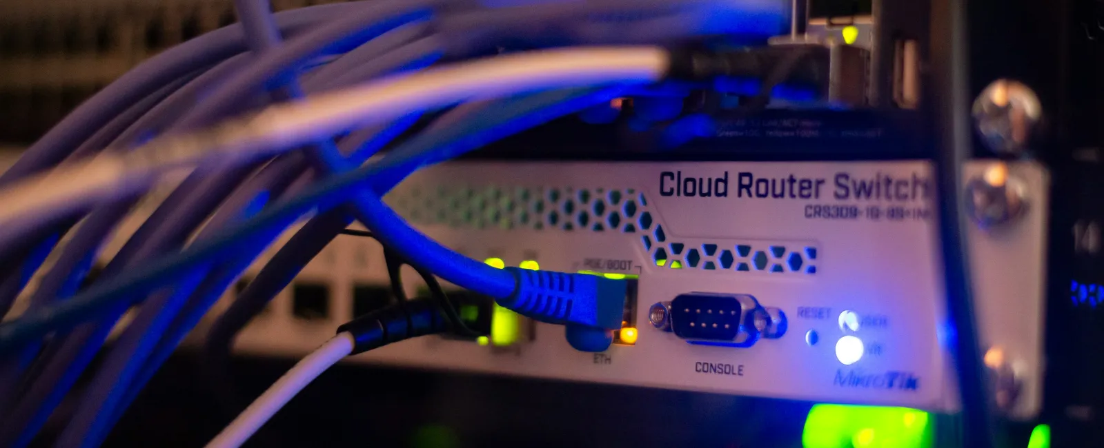 Close-up of a cloud router switch with multiple Ethernet cables connected and LED status lights glowing blue and green.