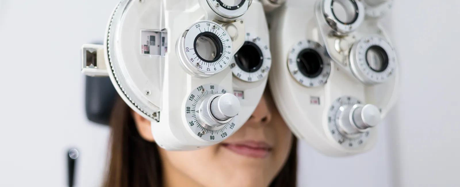 Woman undergoing eye examination with a phoropter device in an optometry clinic close-up.