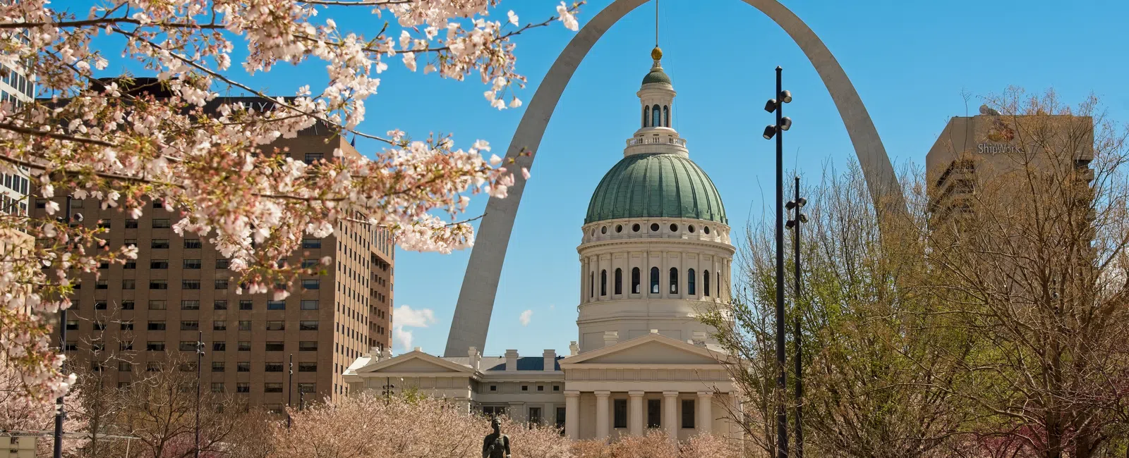 Spring view of St. Louis Arch and Old Courthouse framed by cherry blossoms and clear blue sky