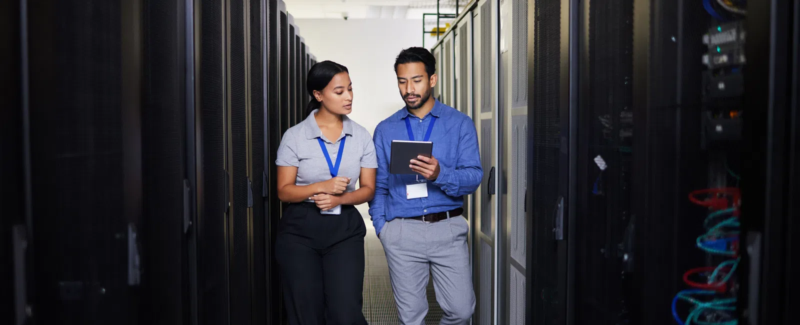 Two IT professionals discussing while walking inside a data center aisle with server racks on both sides.