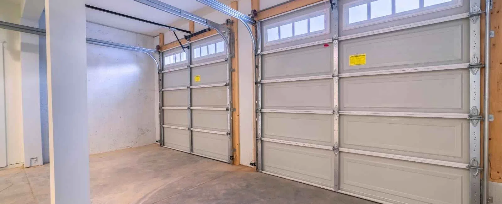 Empty two-car garage with closed white sectional doors and concrete floor under bright lighting