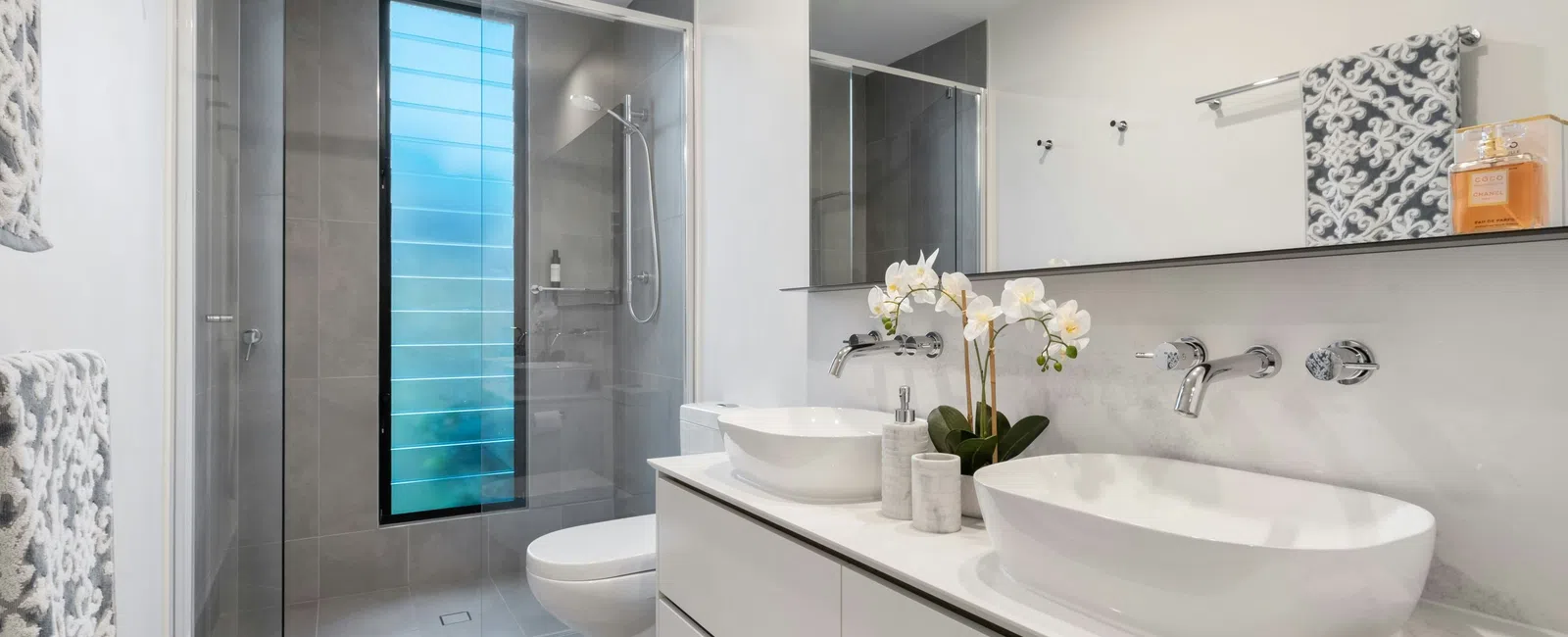 Modern bathroom with double white vessel sinks, a large mirror, glass shower, and gray floor tiles