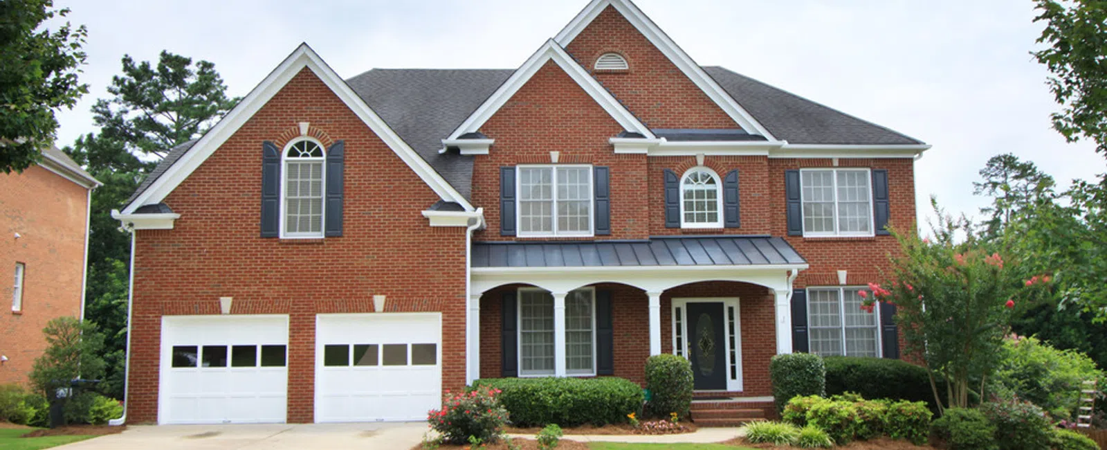 Large two-story brick house with white trim, arched windows, double garage, and well-kept front yard with green lawn.