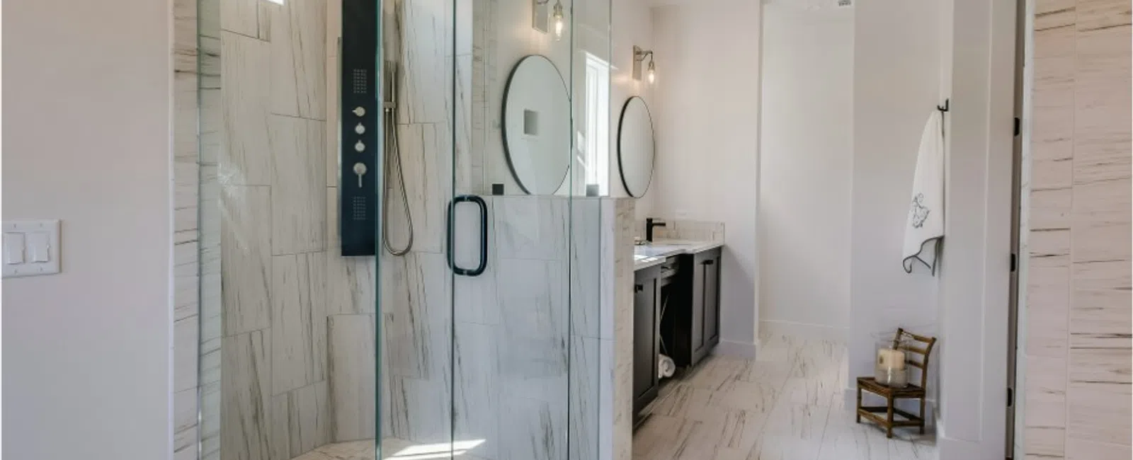 Modern bathroom with glass shower enclosure, marble tile flooring, double vanity, and round mirrors, no overlaid text