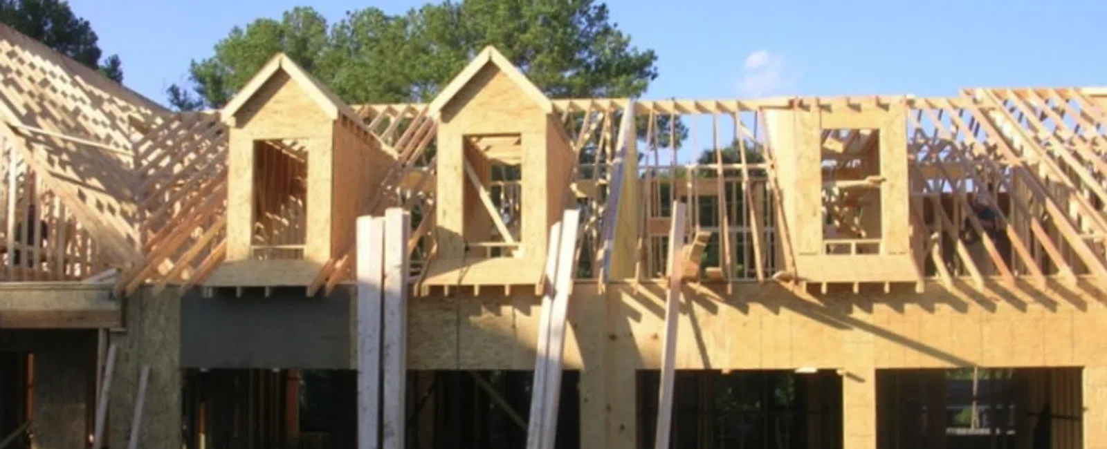 Wooden house frame under construction with roof trusses and dormer windows on a clear sunny day.