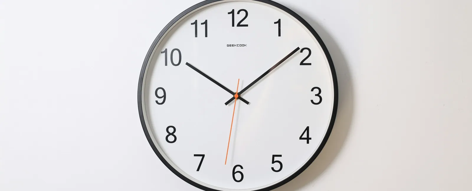 Round wall clock with black frame and hands showing 10:10 on a white background