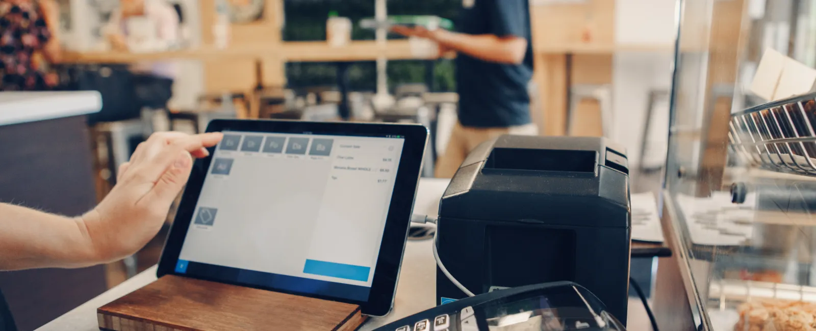 Person using touchscreen point of sale system with card reader and receipt printer in cafe