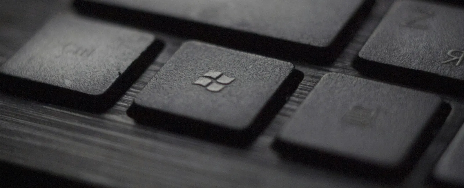 Close-up of a black computer keyboard with a focused Windows key on a dark wood surface.