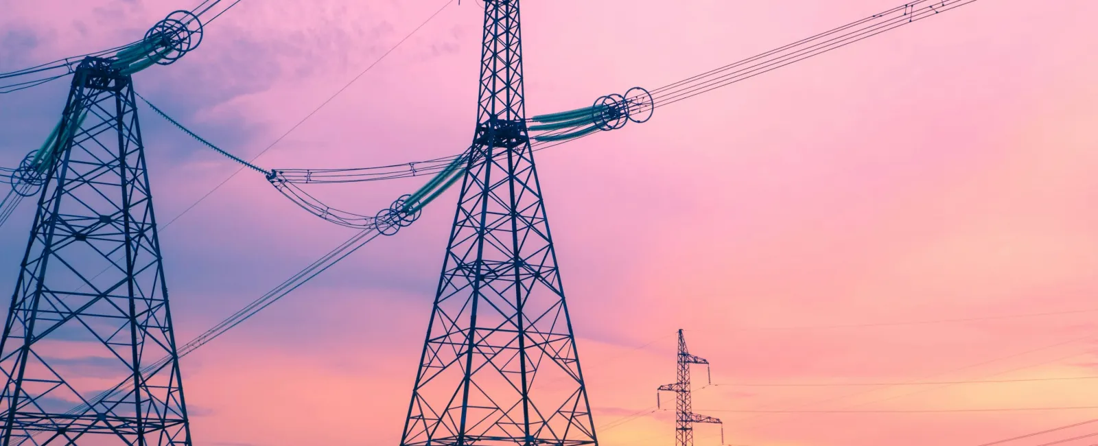 High-voltage power lines and tall transmission towers against a pink and orange sunset sky