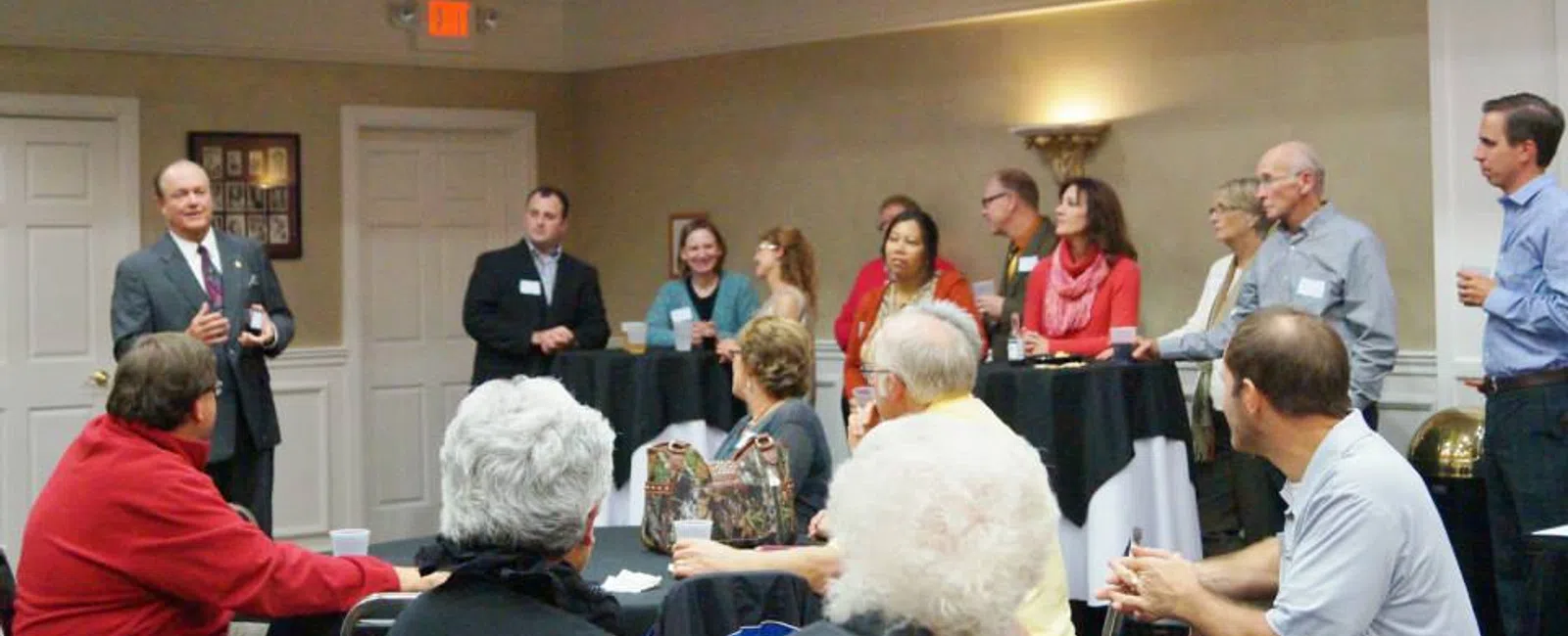 A speaker addressing a seated diverse group of adults in a casual indoor meeting or networking event.