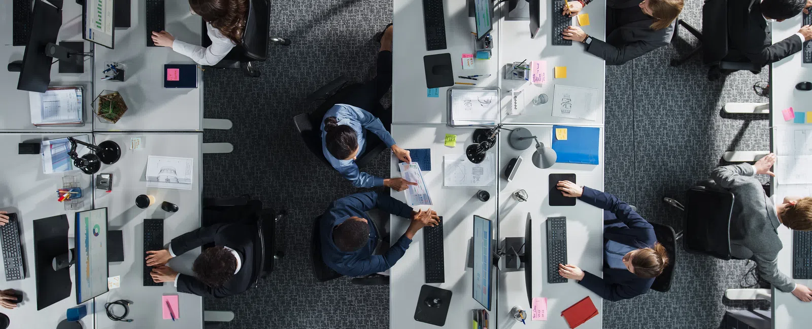 Top-down view of a busy modern office with employees working at desks and collaborating in teams.