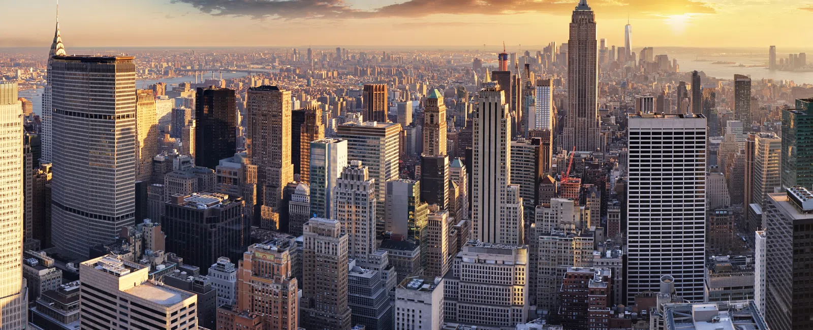 New York City skyline with Empire State Building at sunset, skyscrapers, and partly cloudy sky.
