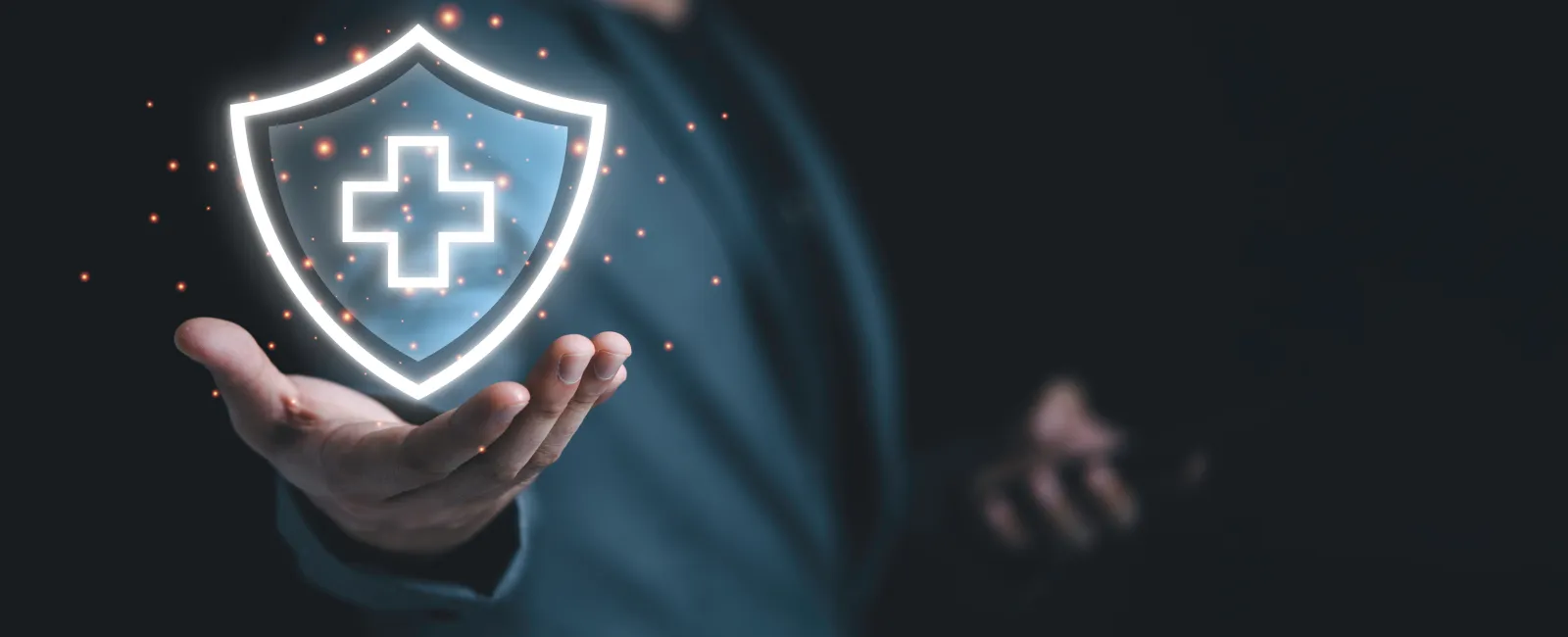Businessman holding glowing shield with medical cross symbol representing health protection and security.