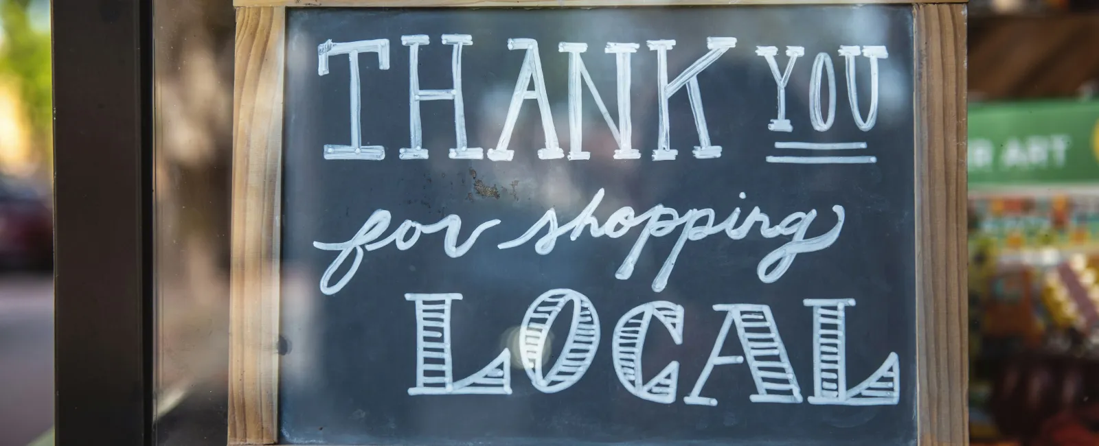 Chalkboard sign with wooden frame saying Thank You for Shopping Local in store window.