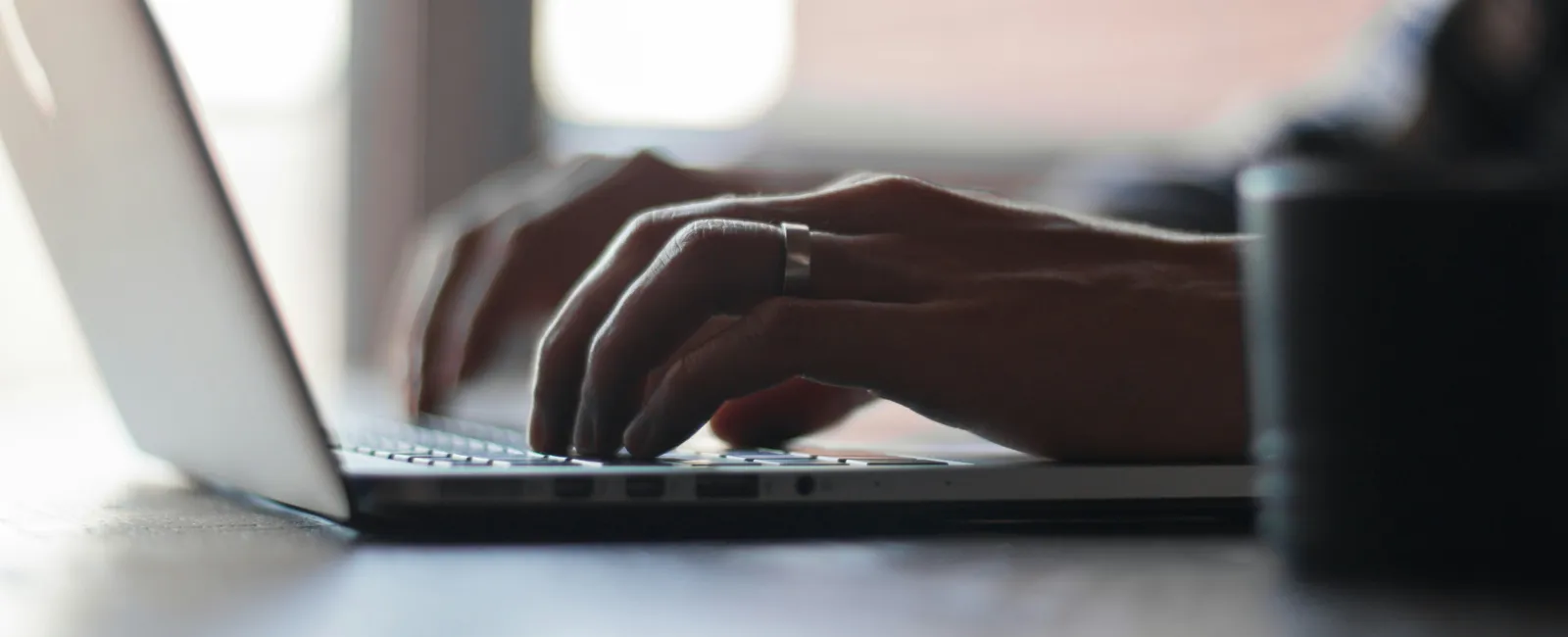 Close-up of hands typing on a laptop keyboard with natural light in a workspace setting.