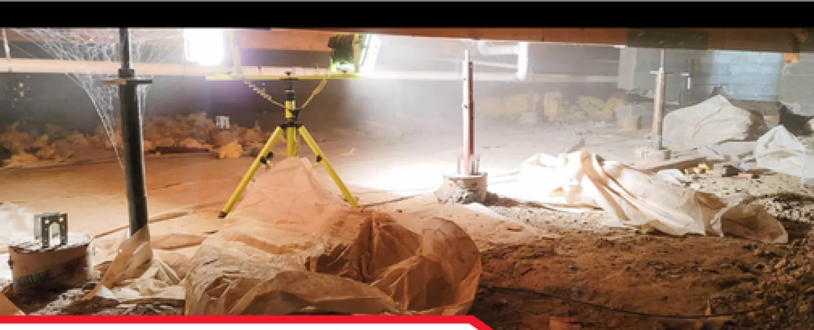 Crawlspace with insulation, support beams, and bright inspection light tripod illuminating the area.