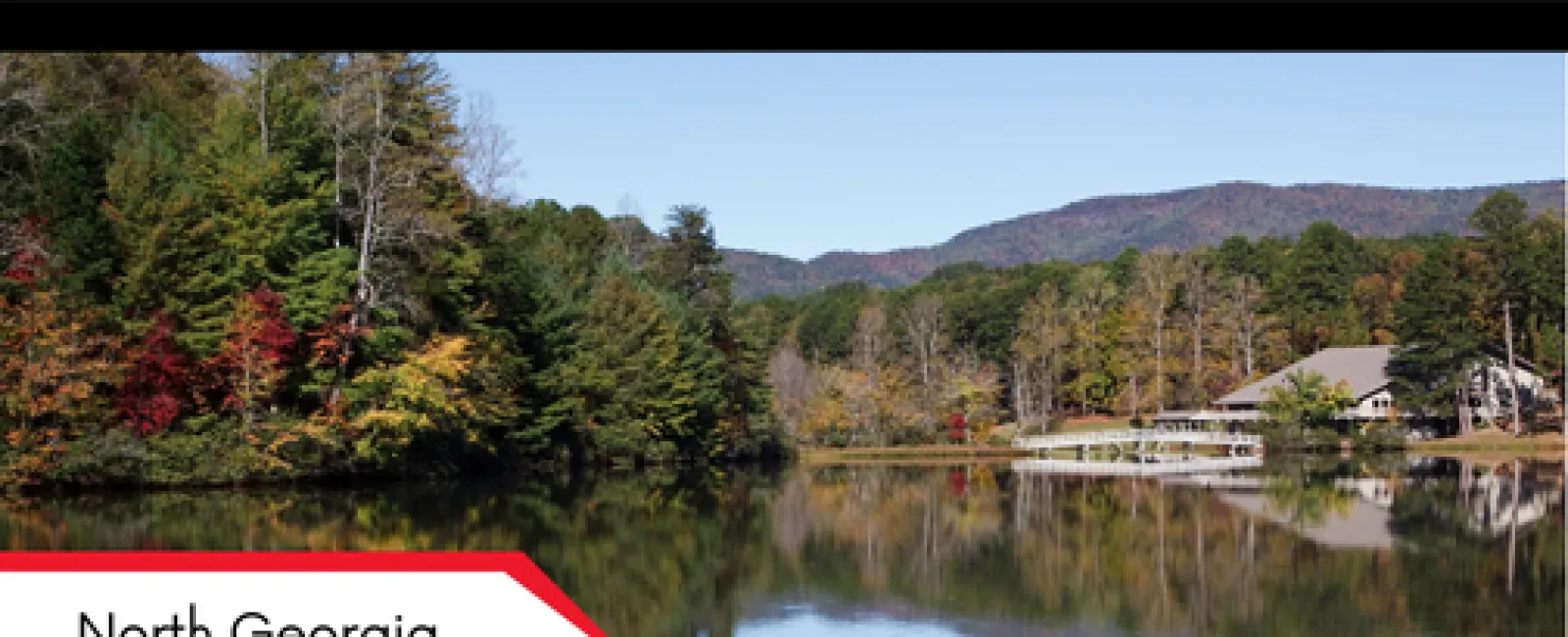 Tranquil lake reflecting autumn trees and distant mountains in North Georgia near a lakeside house.