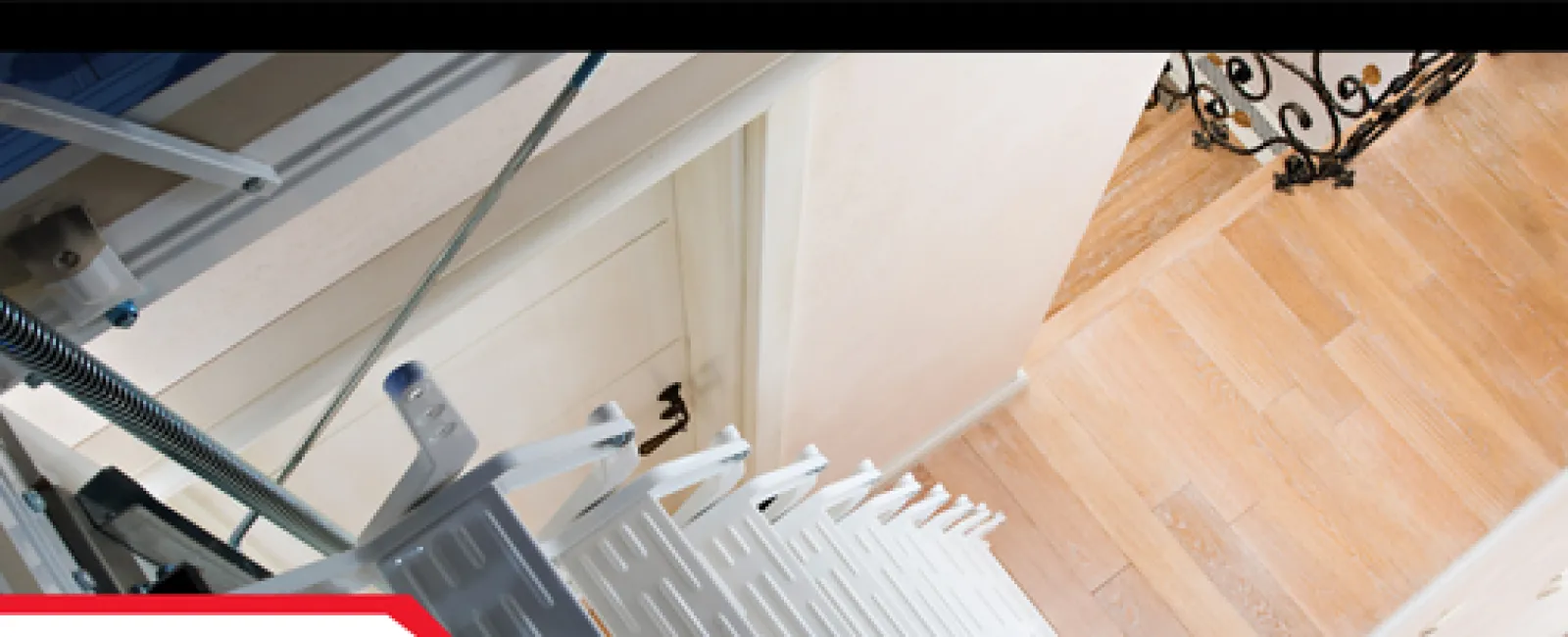 Top view of a foldable attic stairs leading down to a wooden floor landing near a closed door.