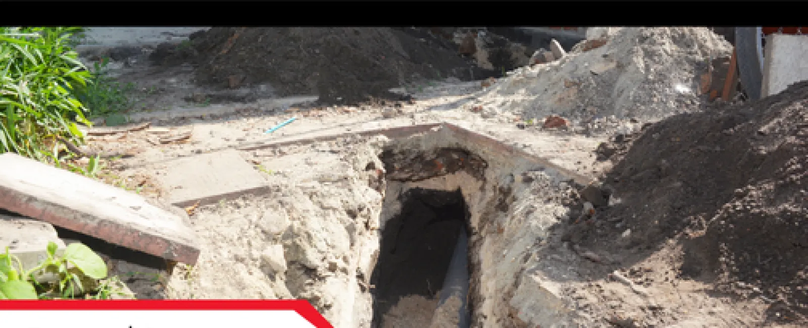 Exposed sewer line in a dug trench for inspection, surrounded by soil and construction debris under daylight.