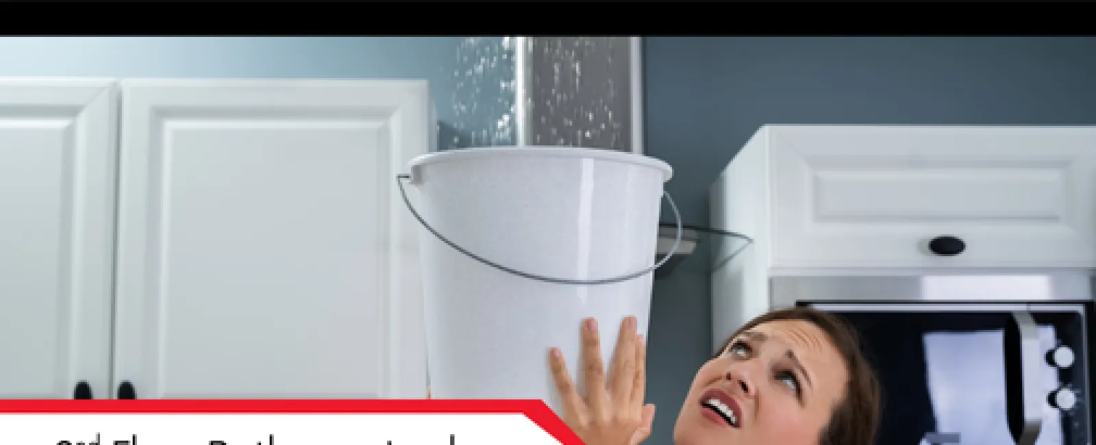 Woman holds bucket under indoor ceiling leak collecting water in modern kitchen with white cabinets and appliances.