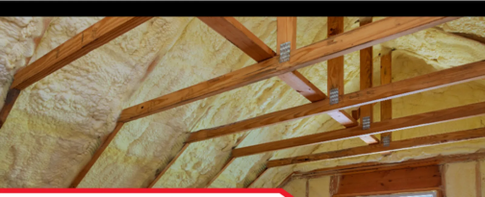 Wooden attic beams and spray foam insulation during a home inspection with natural light from a window.