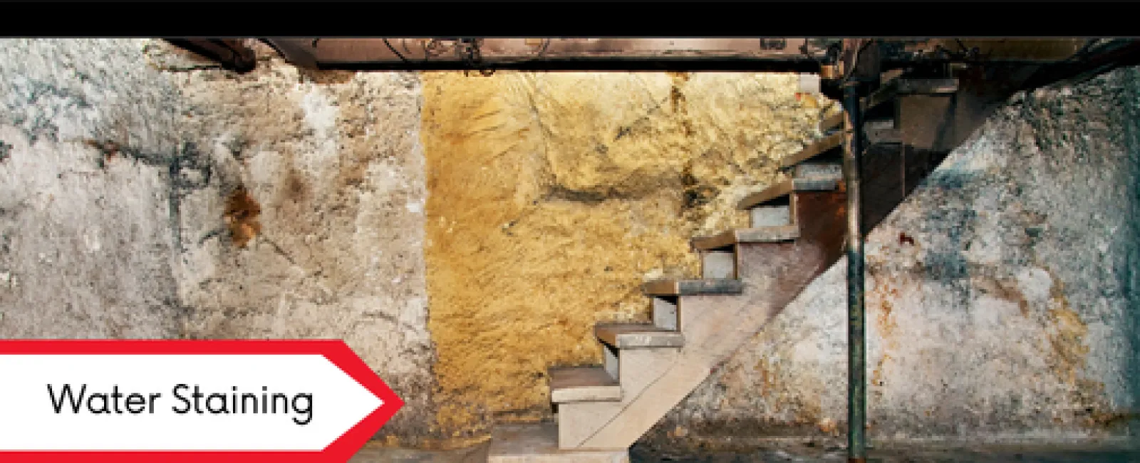 Basement with concrete stairs and walls showing significant water staining and discoloration under pipes.