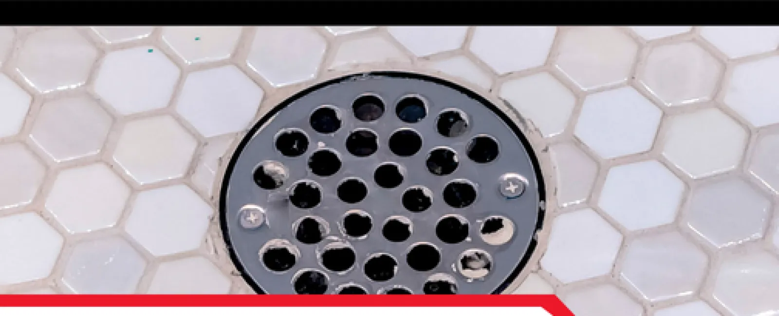 Close-up of a shower drain on hexagonal white tiles highlighting the need for shower drain inspections.