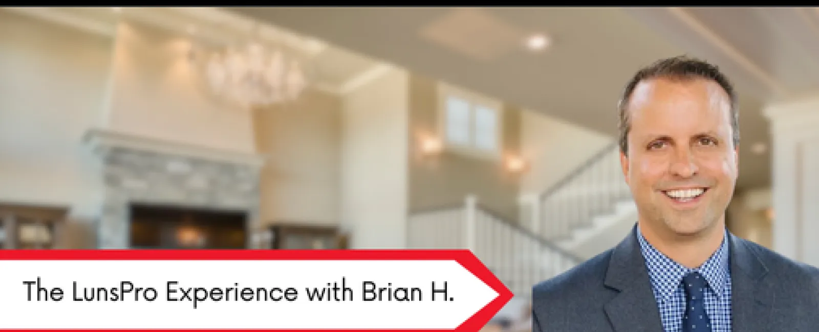 Smiling man in suit stands in front of elegant living room with fireplace and staircase in background