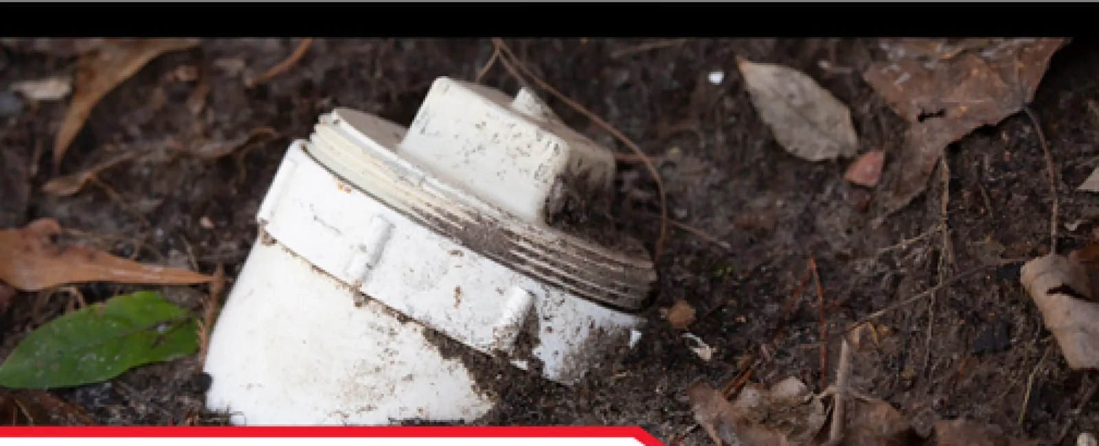 Close-up of main cleanout pipe partially buried in soil and surrounded by leaves for drainage access.