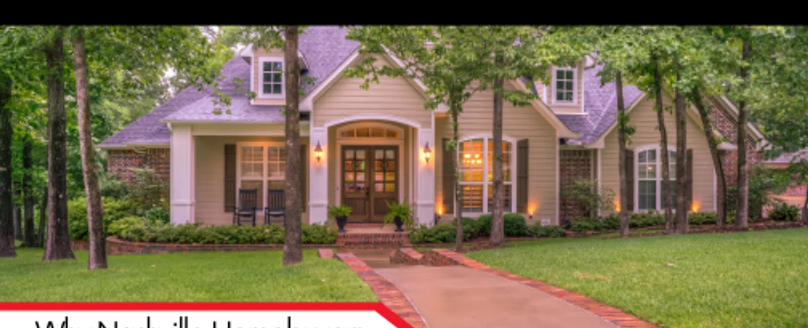 Beautiful suburban house with lit windows and a brick driveway surrounded by trees and greenery at dusk.