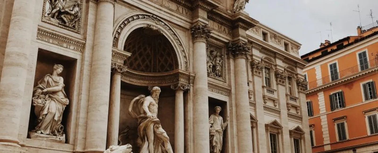 a large stone building with statues with Trevi Fountain in the background