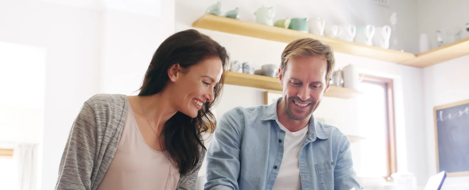 Couple reviewing documents and smiling in a bright modern kitchen with coffee mugs and laptop nearby