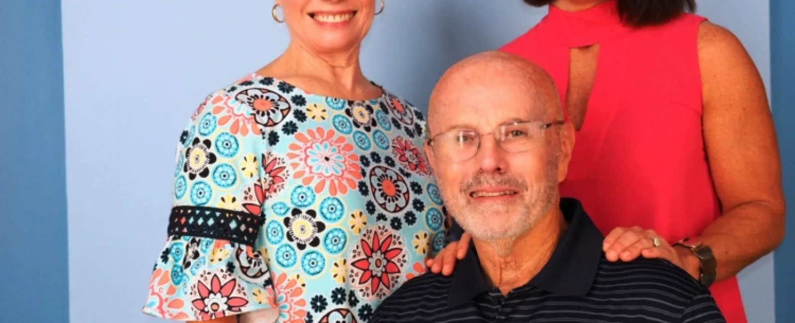 Smiling elderly man with two women standing behind him against a blue background