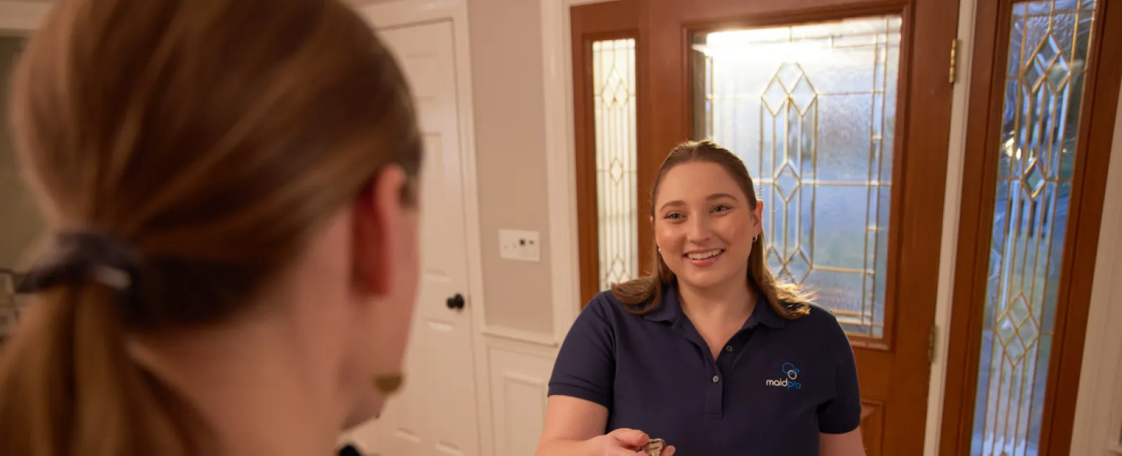 Smiling cleaning service worker handing keys to a woman at a home's front door during a service appointment.