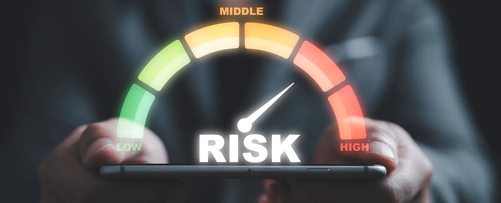 Hand holding smartphone with risk meter indicator showing high risk in red zone on digital interface.