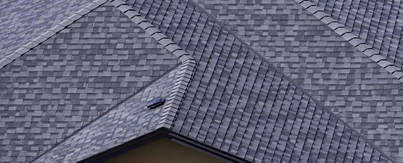 Close-up of a grey shingled house roof with multiple intersecting slopes and vents.