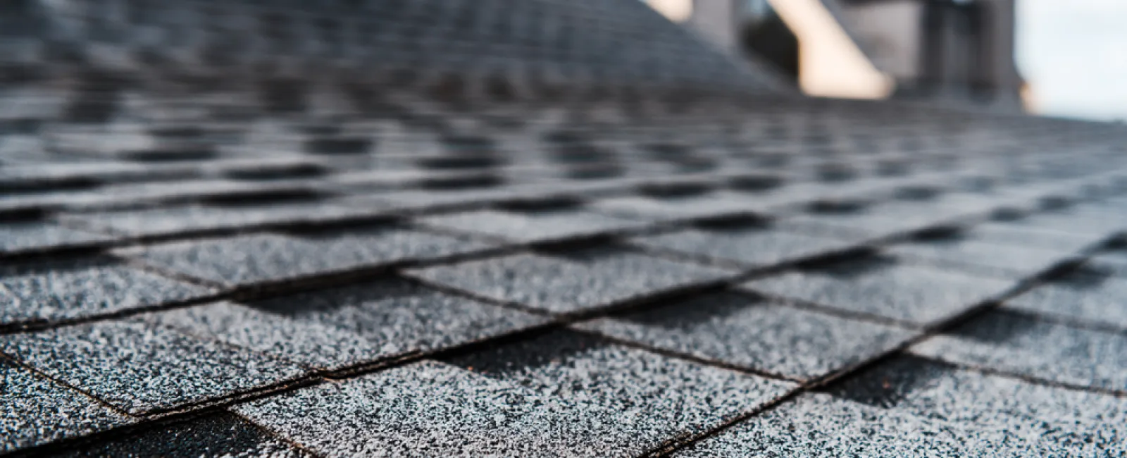 Close-up of black asphalt shingles on a residential roof with a blurred house in the background