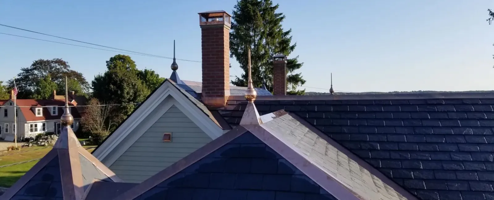 Slate roof with decorative finials and brick chimneys on residential houses under clear blue sky.