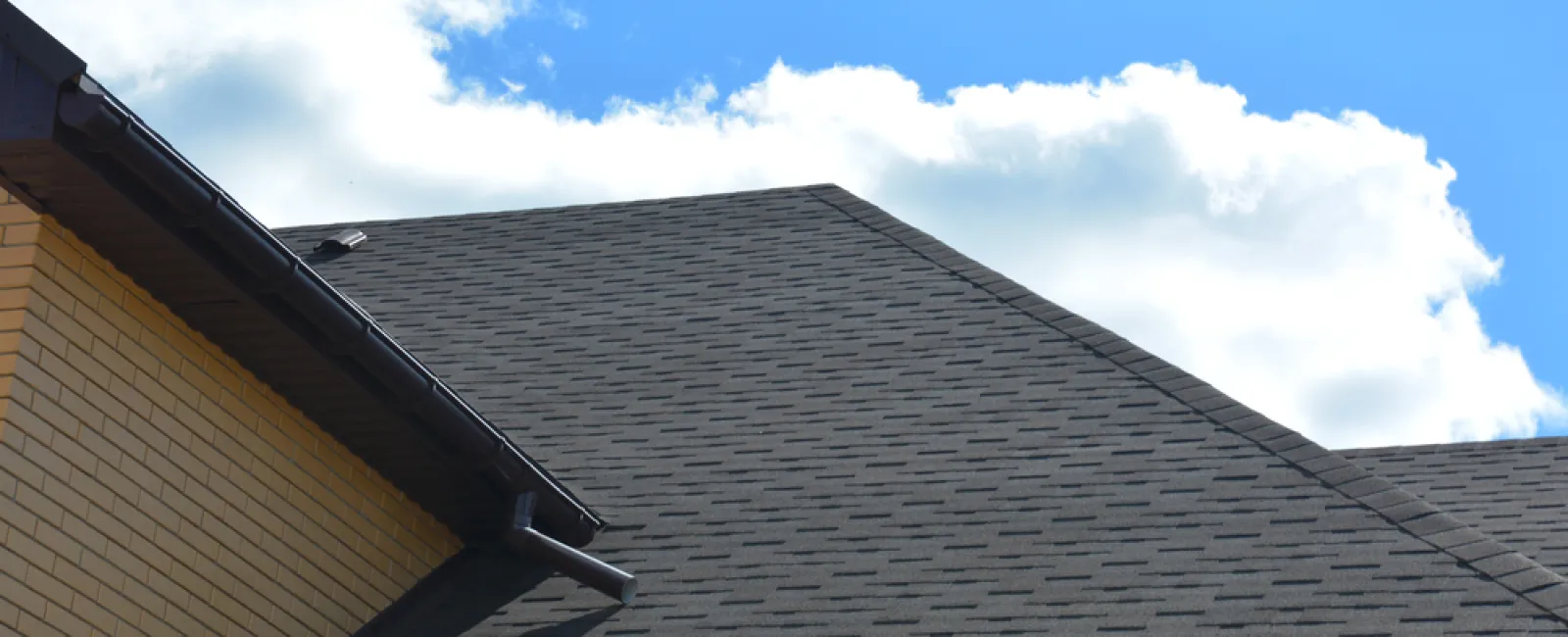 Close-up of a modern house roof with dark asphalt shingles under a blue sky with white clouds