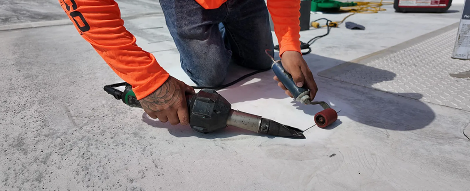 Worker in orange shirt kneeling on concrete using tools for floor repair or sealing outdoors under sunlight