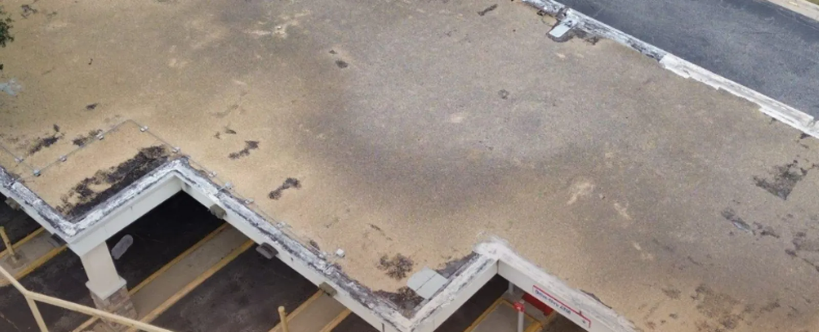 Aerial view of a flat, weathered commercial building roof with faded patches and surrounding parking area.