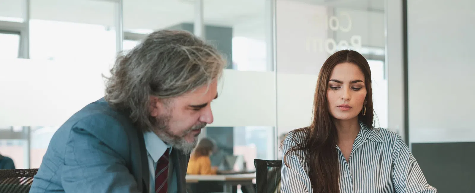 Businessman explains documents to colleague in modern office meeting room during discussion.