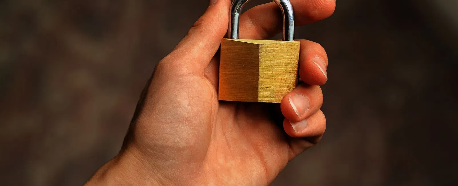 Close-up of a hand holding a small brass padlock with a blurred background for security concept.